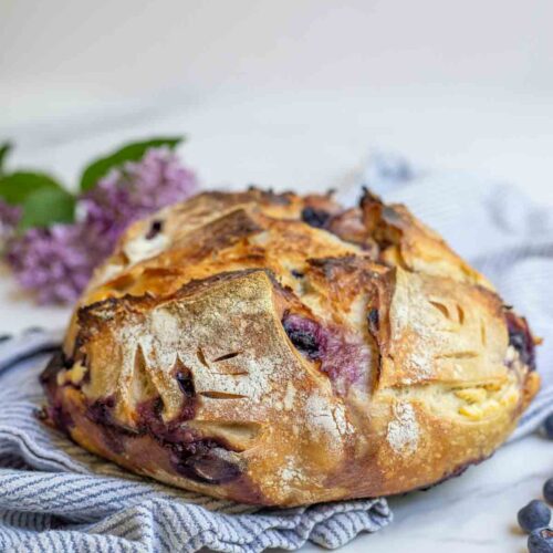 Loaf of sourdough blueberry cream cheese boule on a stripped towel.