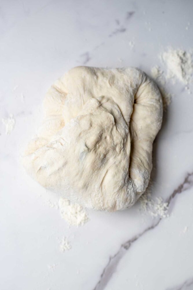 Folding sourdough blueberry cream cheese dough up and into the center on a countertop.