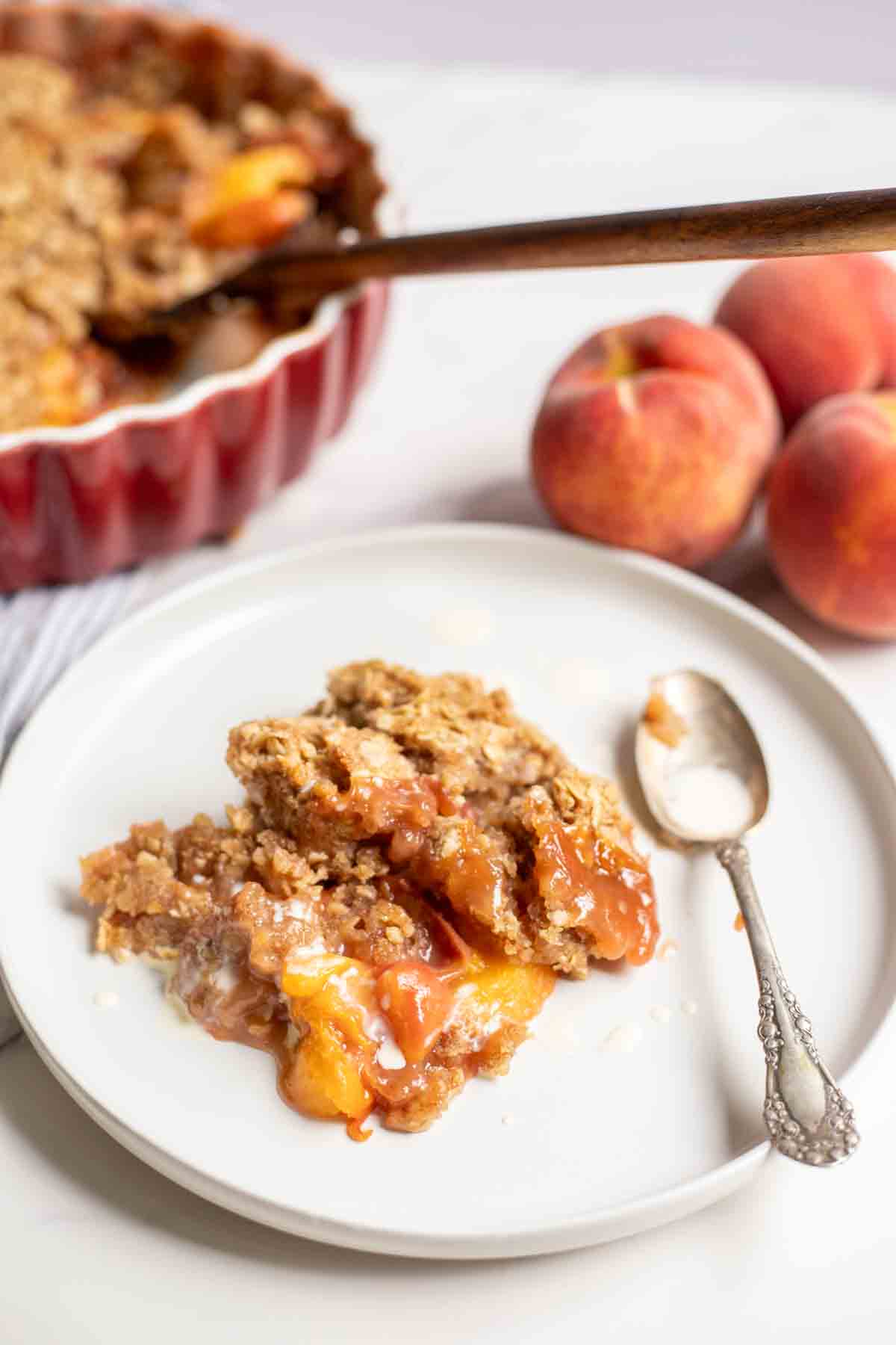 Sourdough peach crisp on a white plate with peaches and a pie plate with more crisp in the background.
