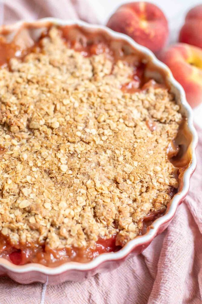 sourdough peach crisp in a baking dish on a pink towel.