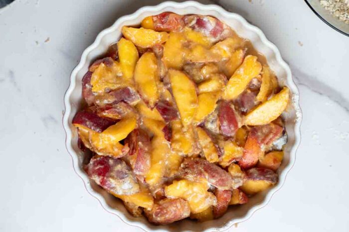 Sliced peaches tossed with sugar, flour, and cinnamon in a deep pie dish.