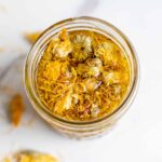 Overhead photo of a jar of calendula oil with dried calendula in it.