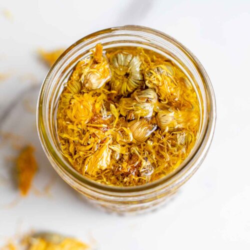 Overhead photo of a jar of calendula oil with dried calendula in it.
