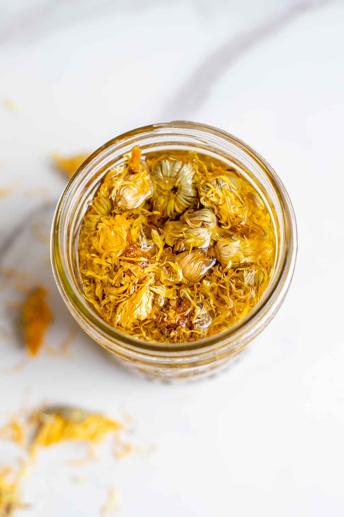 Overhead photo of a jar of calendula oil with dried calendula in it.