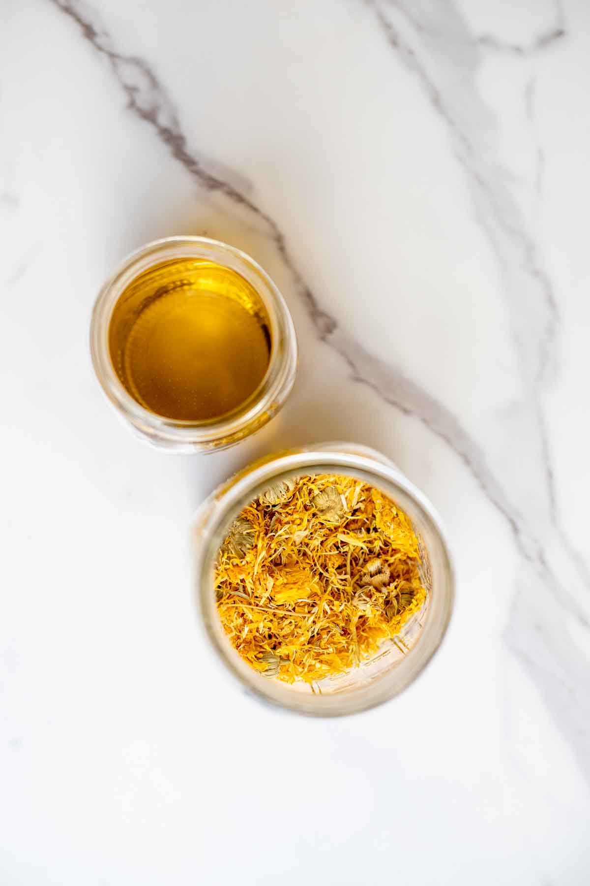 a jar of oil and a jar of dried flowers on a countertop.