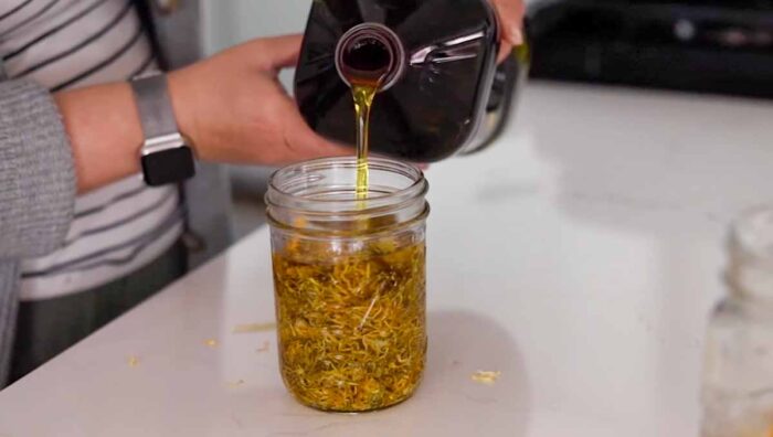 Pouring oil into a mason jar with calendula oil.