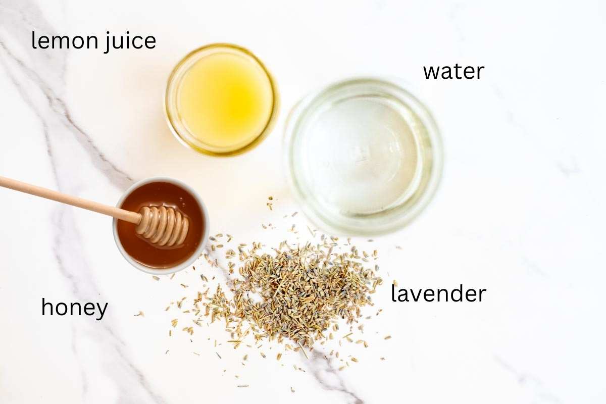 jar of lemon juice and water, dried lavender buds, and a small bowl of honey with a honey scoop on a countertop.