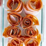 Peach leather rolled up in a glass dish with peaches in the background.