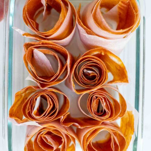 Peach leather rolled up in a glass dish with peaches in the background.
