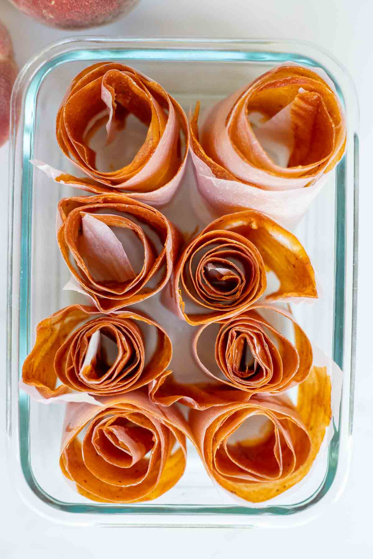 Peach leather rolled up in a glass dish with peaches in the background.