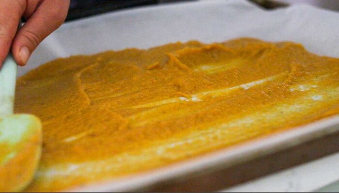 Spreading peach puree onto a parchment lined baking sheet.