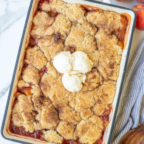 Sourdough peach cobbler in a baking dish topped with ice cream.