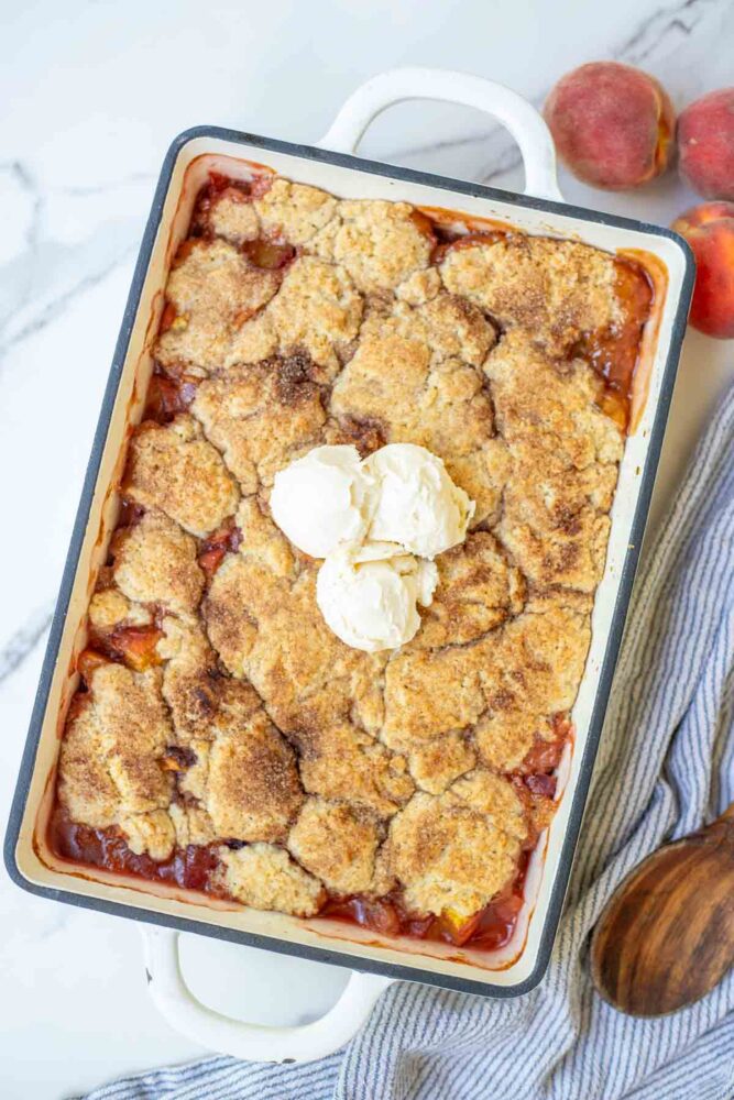 Sourdough peach cobbler in a baking dish topped with ice cream.