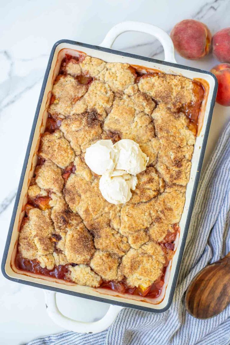 Sourdough peach cobbler in a baking dish topped with ice cream.