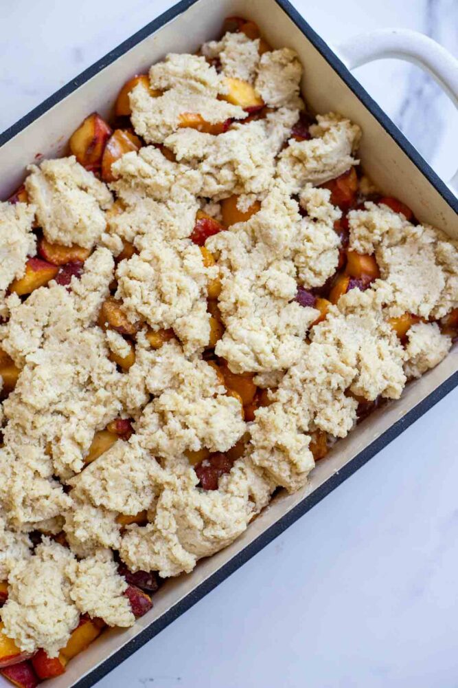 Assembled peach cobbler with raw dough dropped on top.