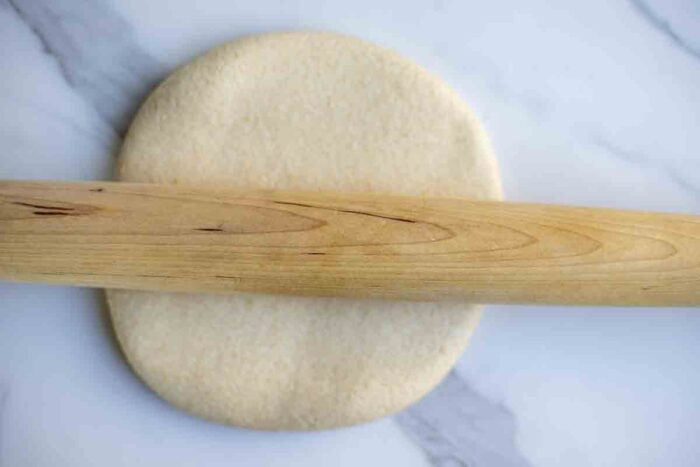 Rolling out sourdough whole wheat pizza dough on a marble countertop.