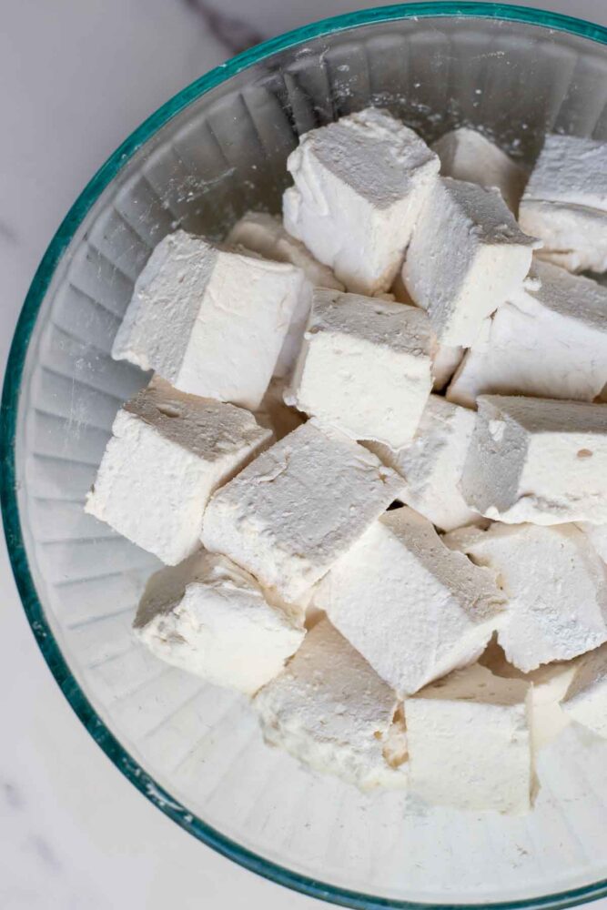 Homemade marshmallows coated with powdered sugar mixture in a bowl.