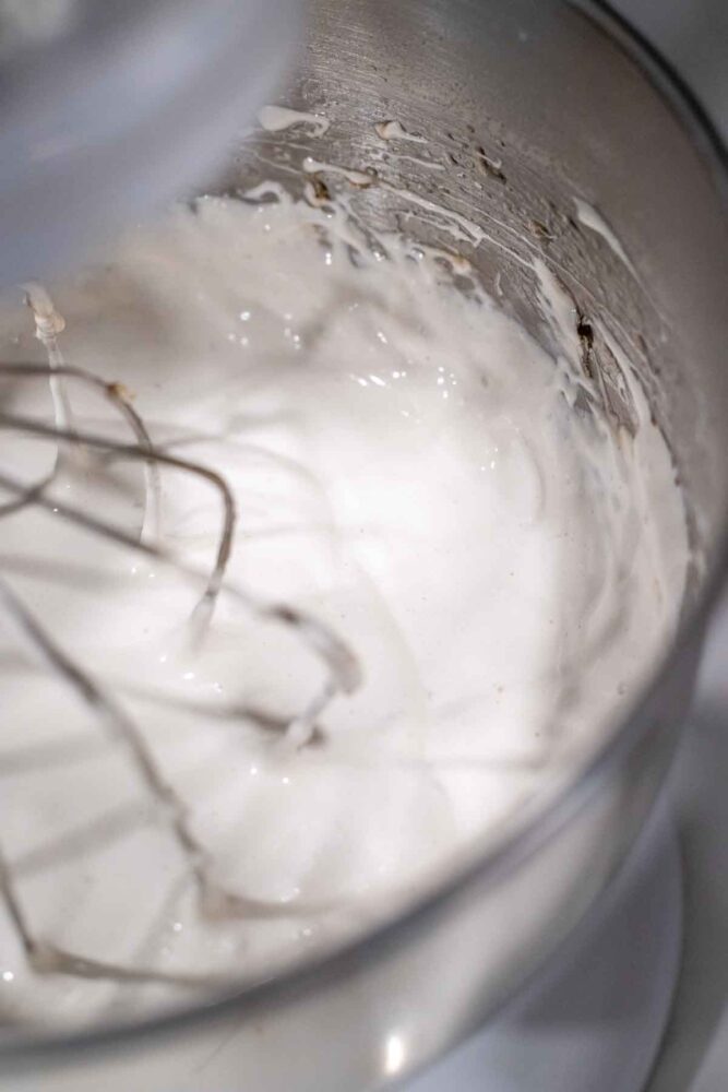 Adding vanilla to marshmallow fluff in a stand mixer bowl.