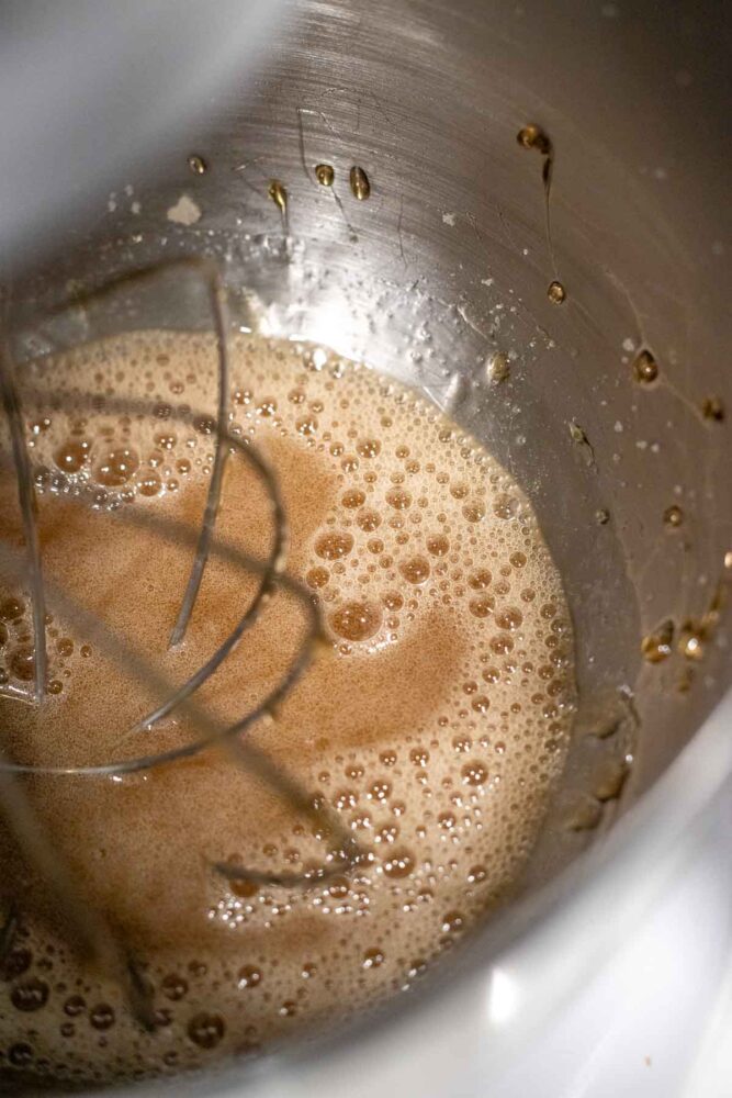Mixing sugar water solution into softened gelatin in a stand mixer bowl with balloon whisk.