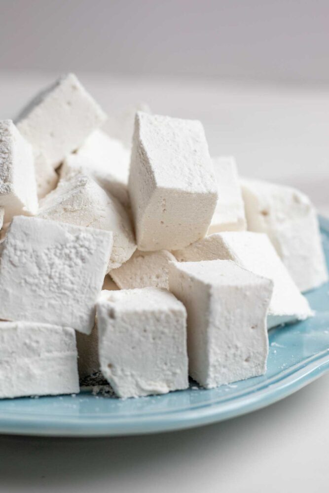 Homemade marshmallows stacked on a blue plate.