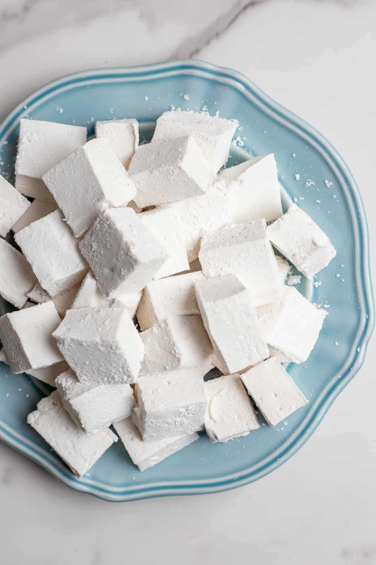 Overhead photo of homemade marshmallows stacked on a blue plate.
