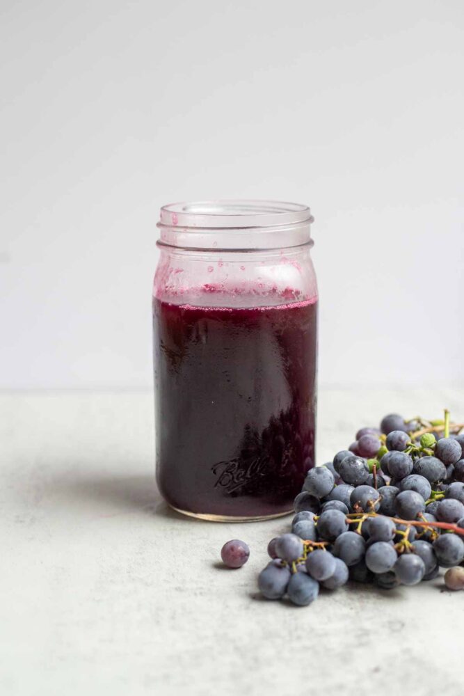 jar of homemade grape juice with a bunch of grapes in front of the jar.
