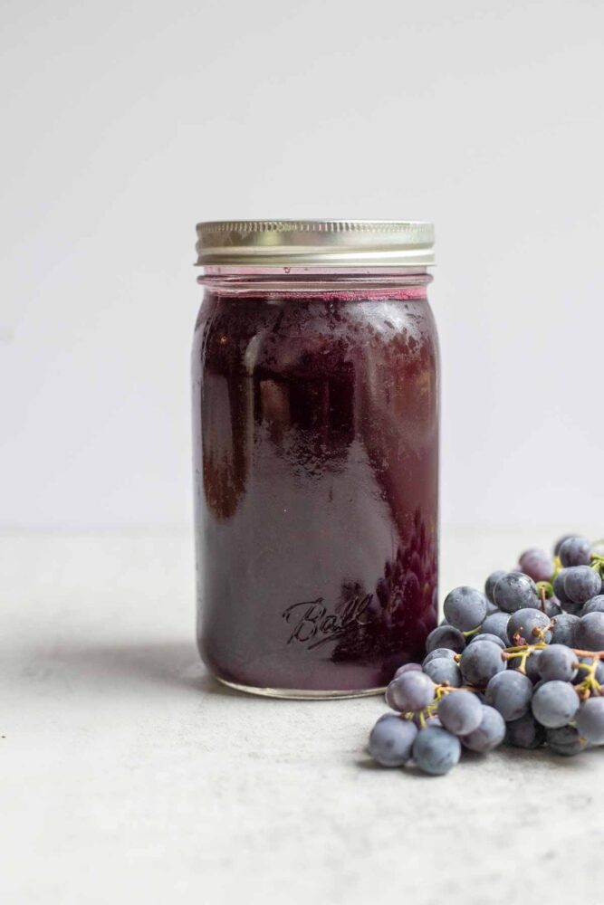 Canned grape juice in a quart jar with grapes in front of the jar.