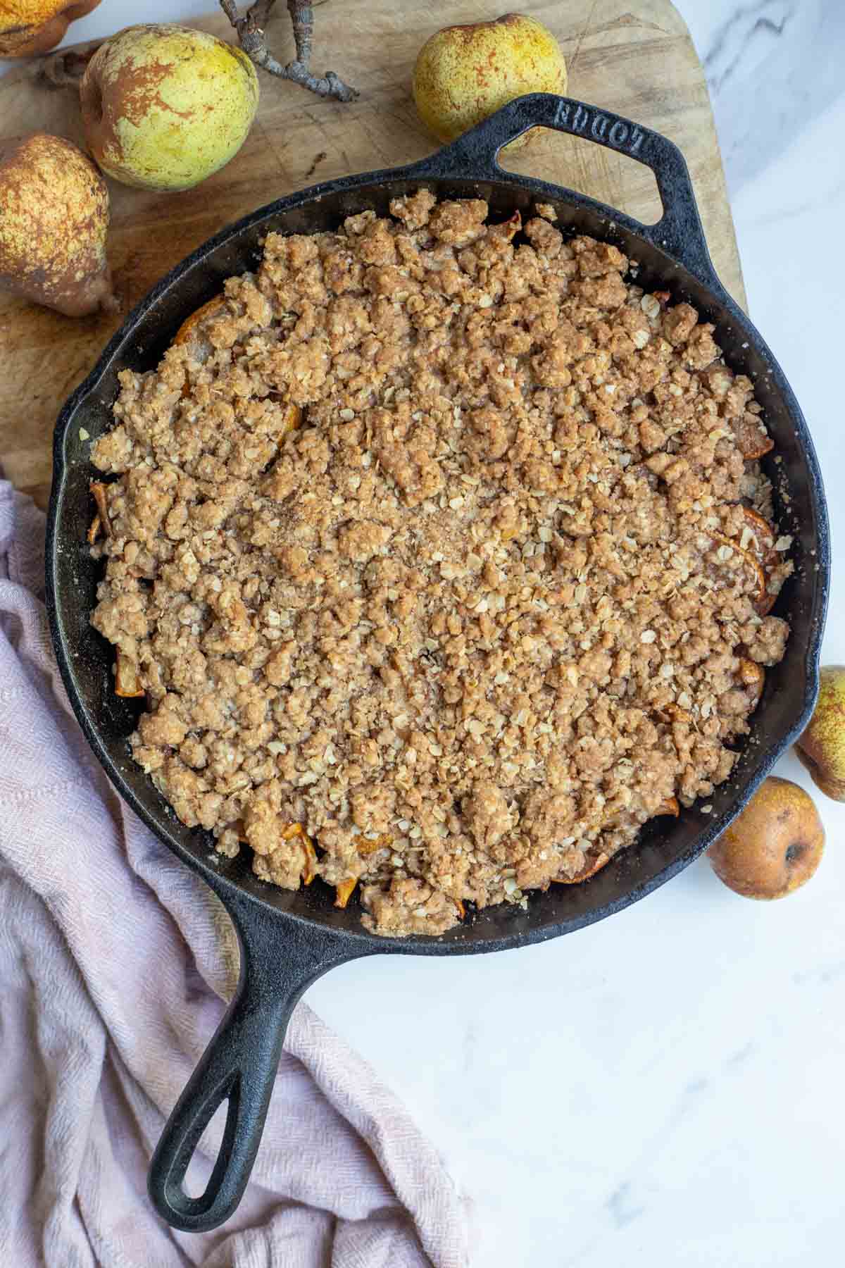 Pear crisp right out of the oven in a cast iron skillet. Pears surround the skillet.