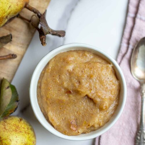 Pear sauce in a small bowl next to a cutting board with more pairs.