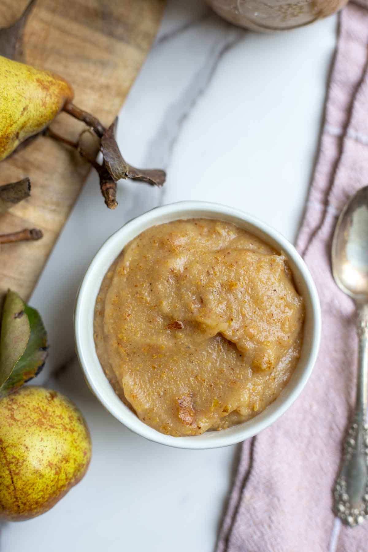 Pear sauce in a small bowl next to a cutting board with more pairs.