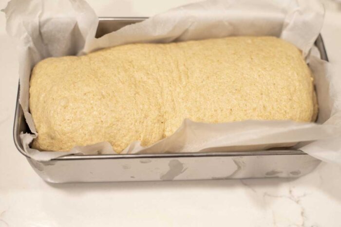Shaped sandwich bread dough in a parchment lined loaf pan.
