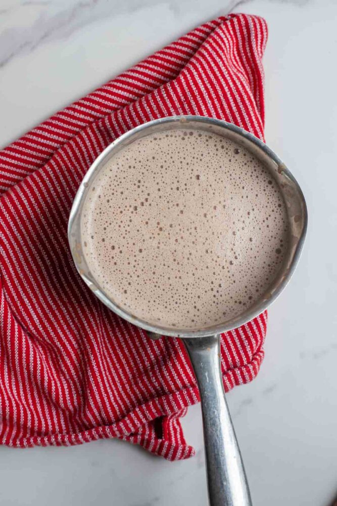 Hot chocolate mixed together in a saucepan on a red stripped towel.