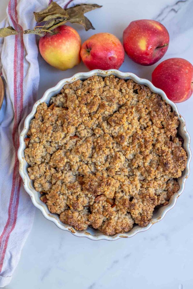 Freshly baked sourdough apple crisp in a baking dish surrounded by home grown apples.