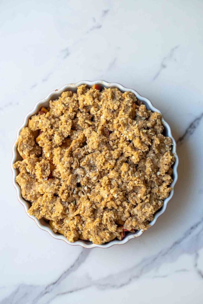Sourdough oat crumble toppings spread evenly over apple filling in a baking dish.
