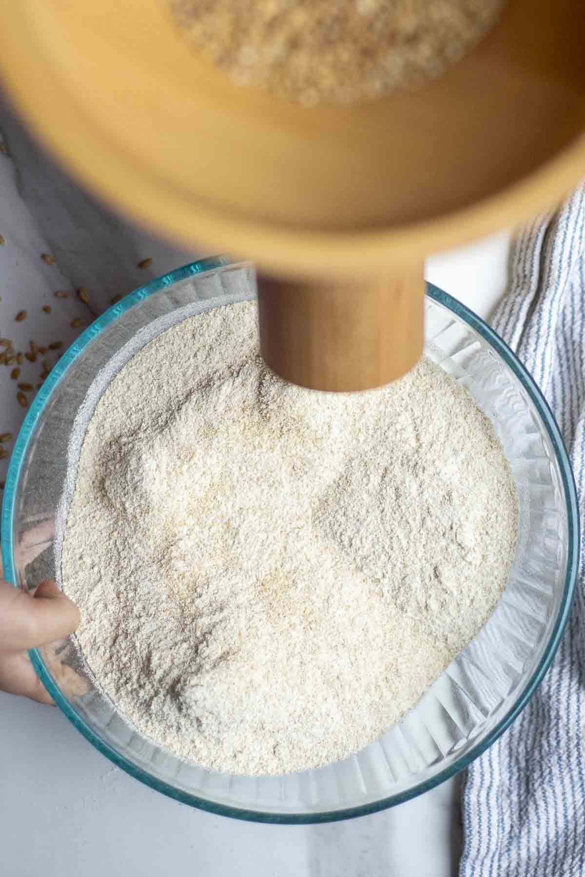 Glass bowl under a grain mill with flour collected.