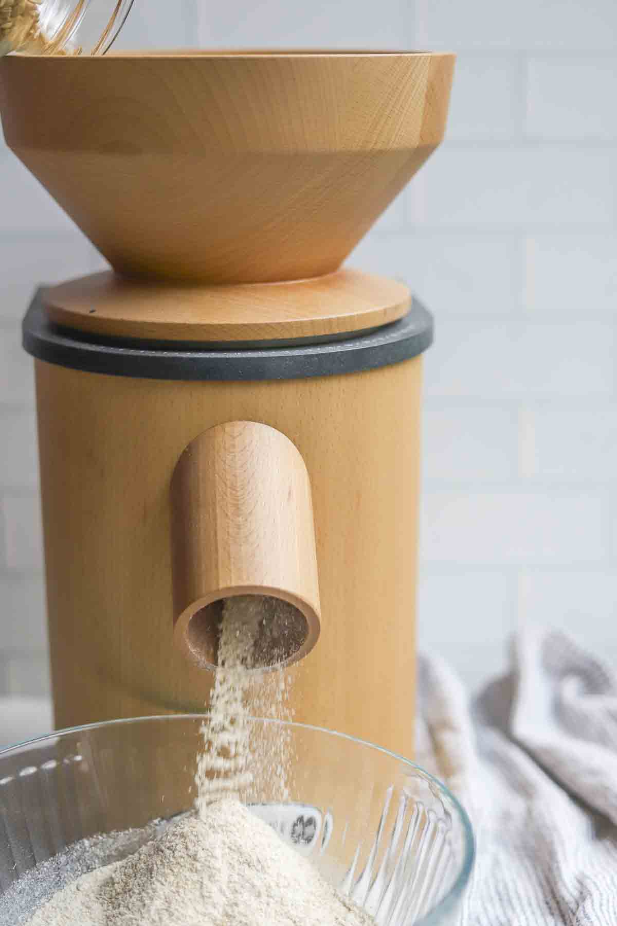 Pouring wheat berries in to a mill. the flour is being added to a glass bowl.