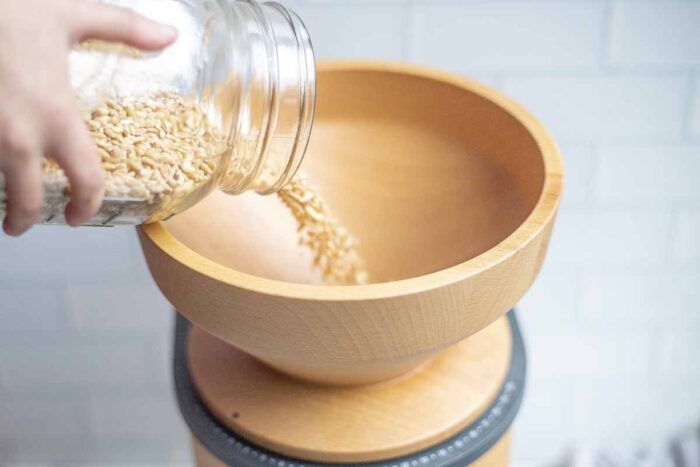 Pouring wheat berries into a grain mill hopper.