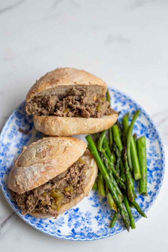 Two Italian beef sandwiches on a blue and white plate with asparagus.