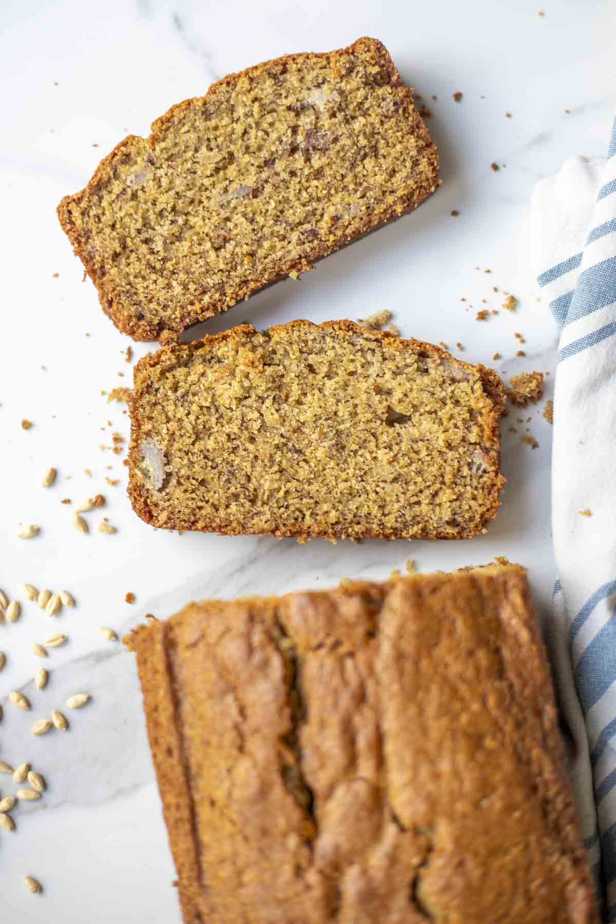 Two slices of whole wheat sourdough banana bread on a countertop with the rest of the loaf at the bottom.