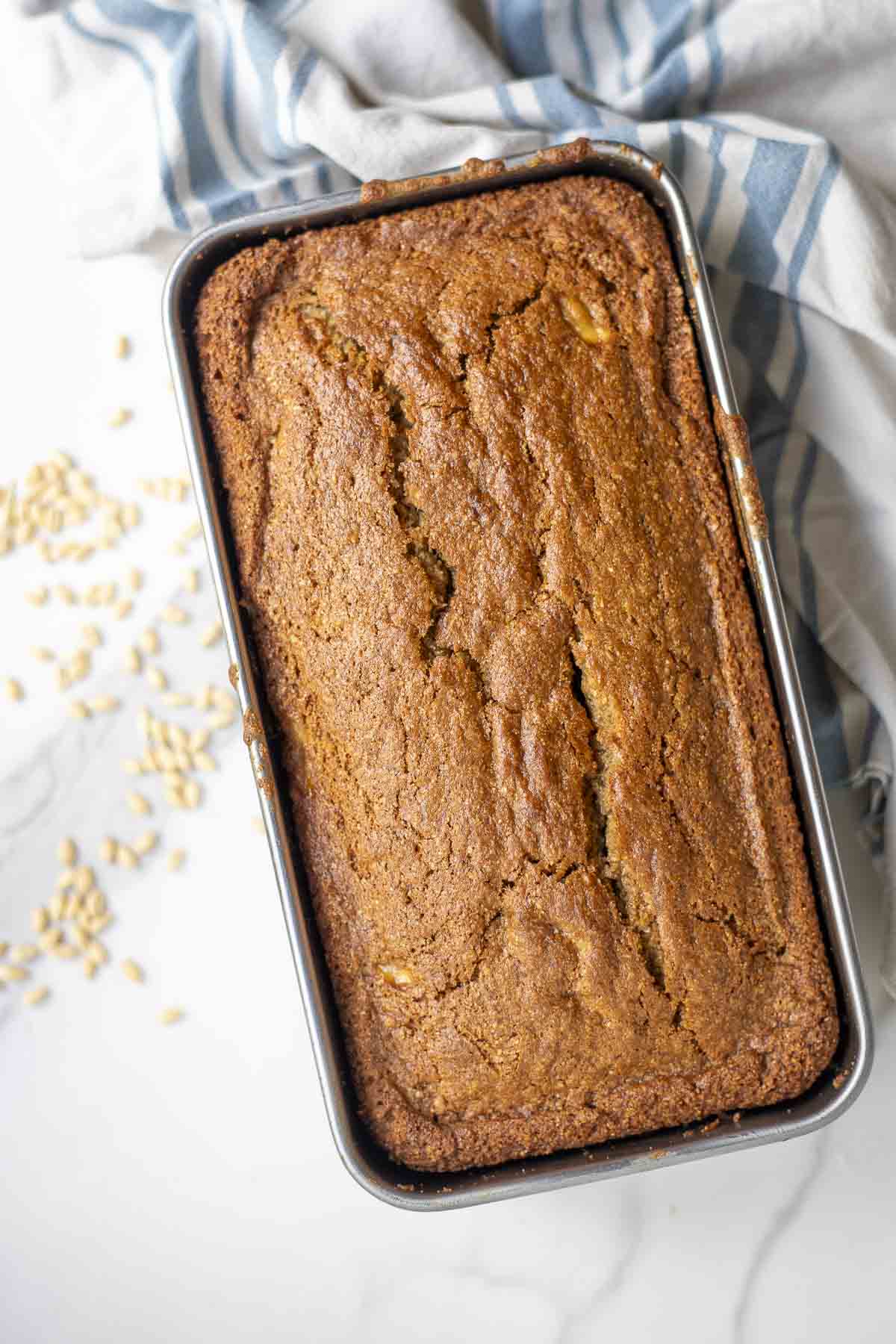 Whole Wheat sourdough banana bread with fresh milled flour baked in a baking pan on a white countertop with a stripped towel.