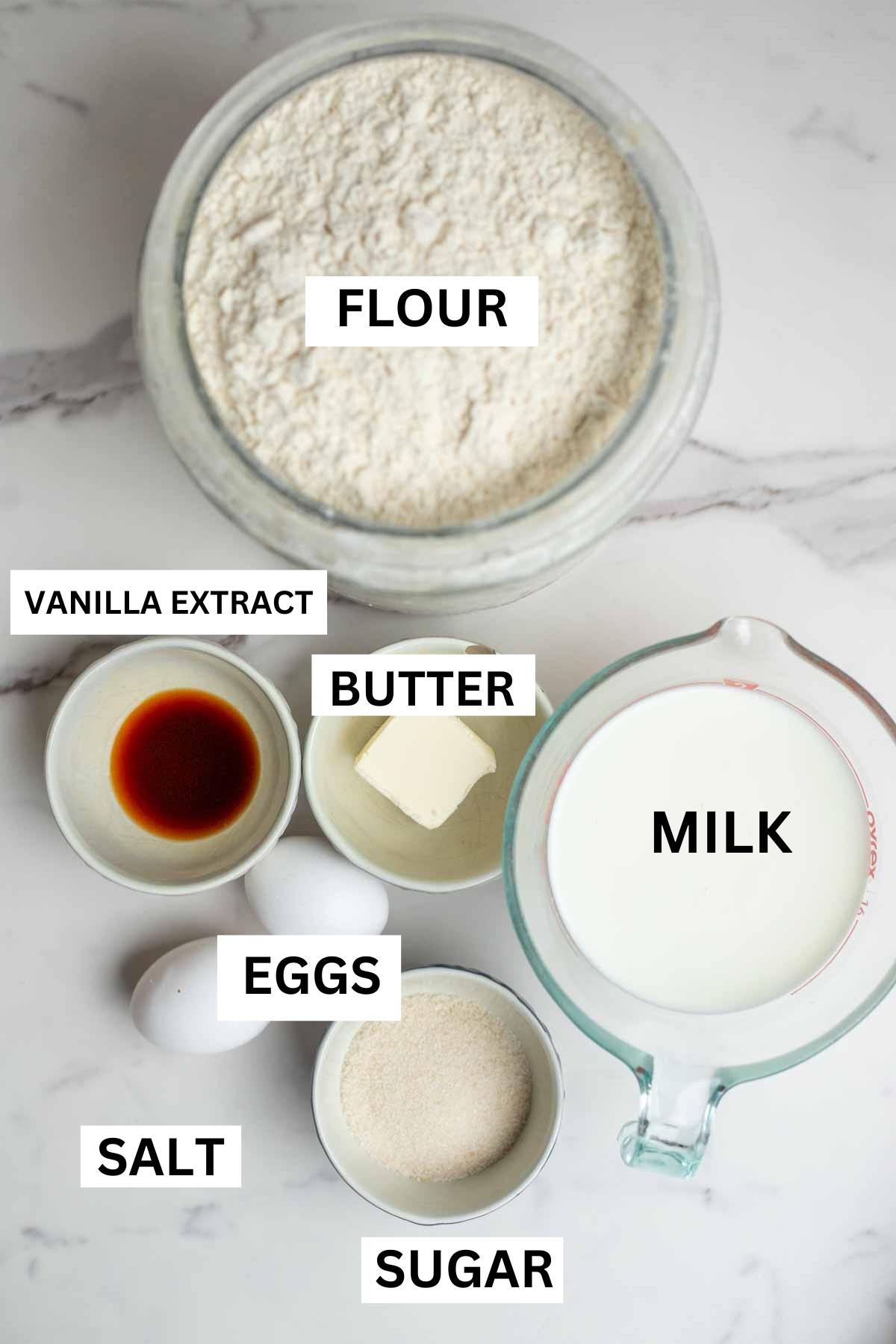 Bowls of flour, butter, sugar, vanilla extract, milk, eggs and salt are also on the countertop.