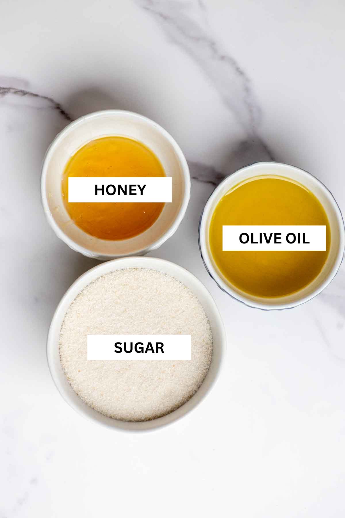 three small bowls with honey, olive oil, and sugar sitting on a countertop.
