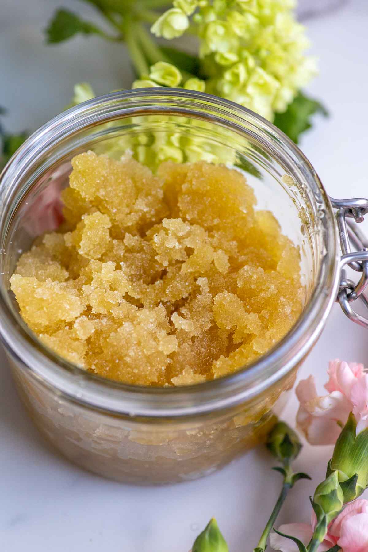 Close up picture of honey sugar scrub in a glass jar surrounded by flowers.