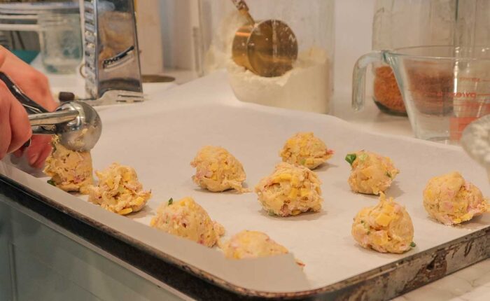 Placing biscuit dough onto a parchment lined baking sheet with an ice cream scoop.