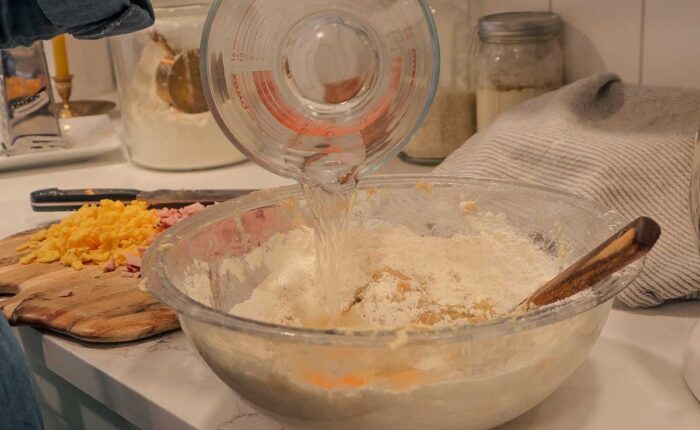 Pouring water into a bowl with dry ingredients, melted butter, and eggs.