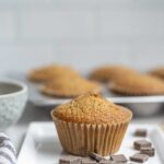 Whole wheat sourdough chocolate chip muffin on a plate surrounded by chocolate chips with more muffins in the background.