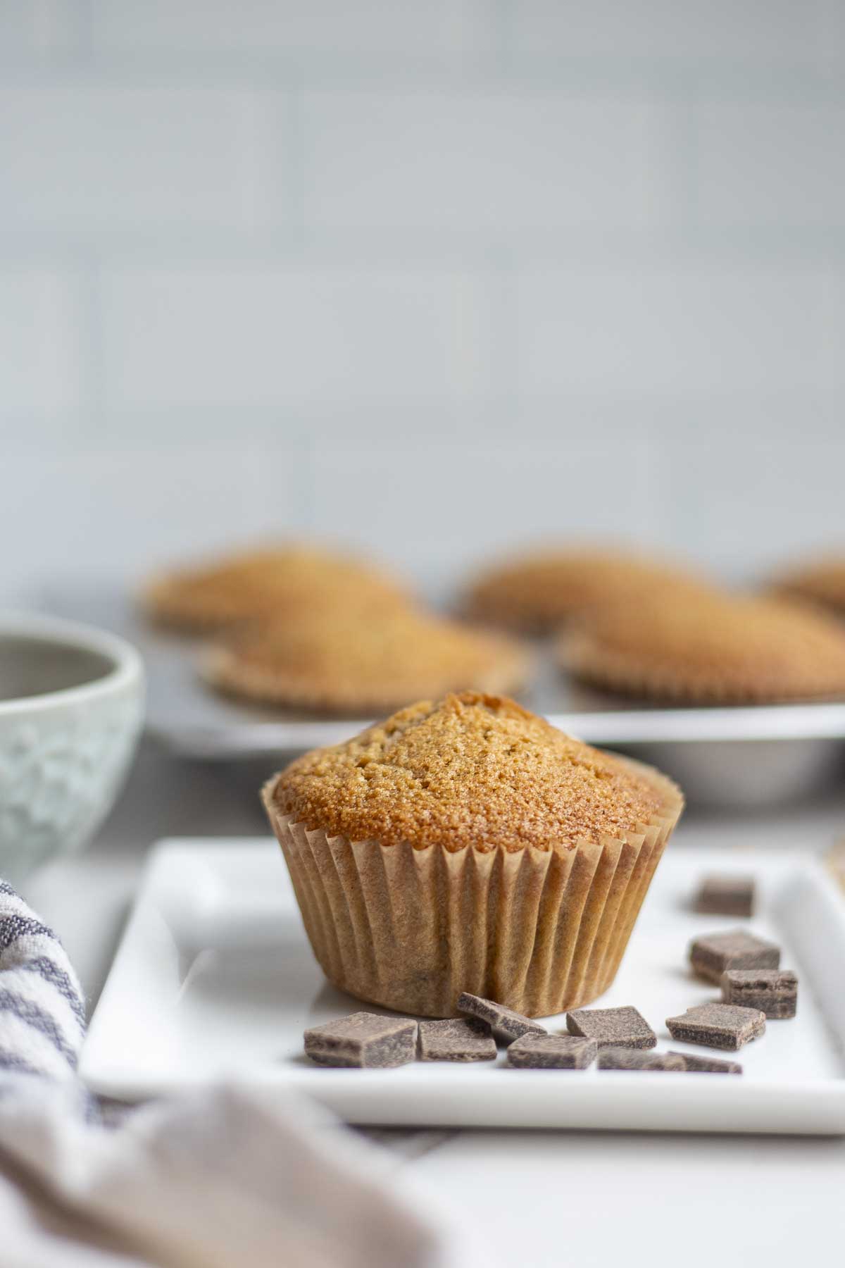 Whole wheat sourdough chocolate chip muffin on a plate surrounded by chocolate chips with more muffins in the background.