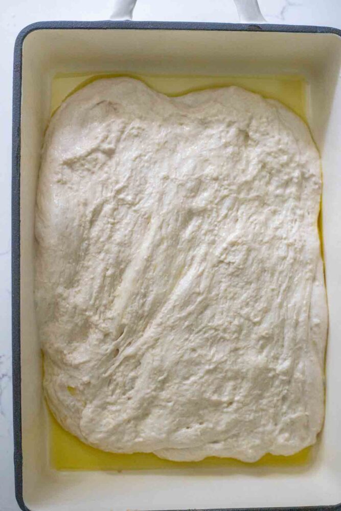 Focaccia dough spread out at the bottom of baking dish covered with olive oil.