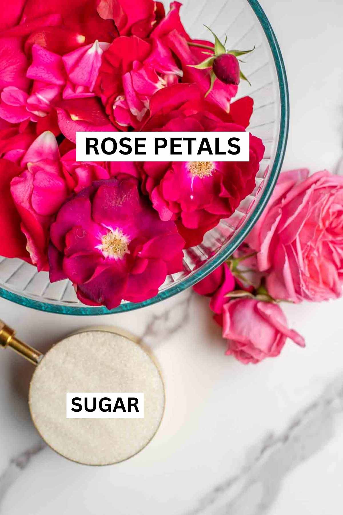 A bowl of rose petals and a measuring cup of sugar on a marble countertop.