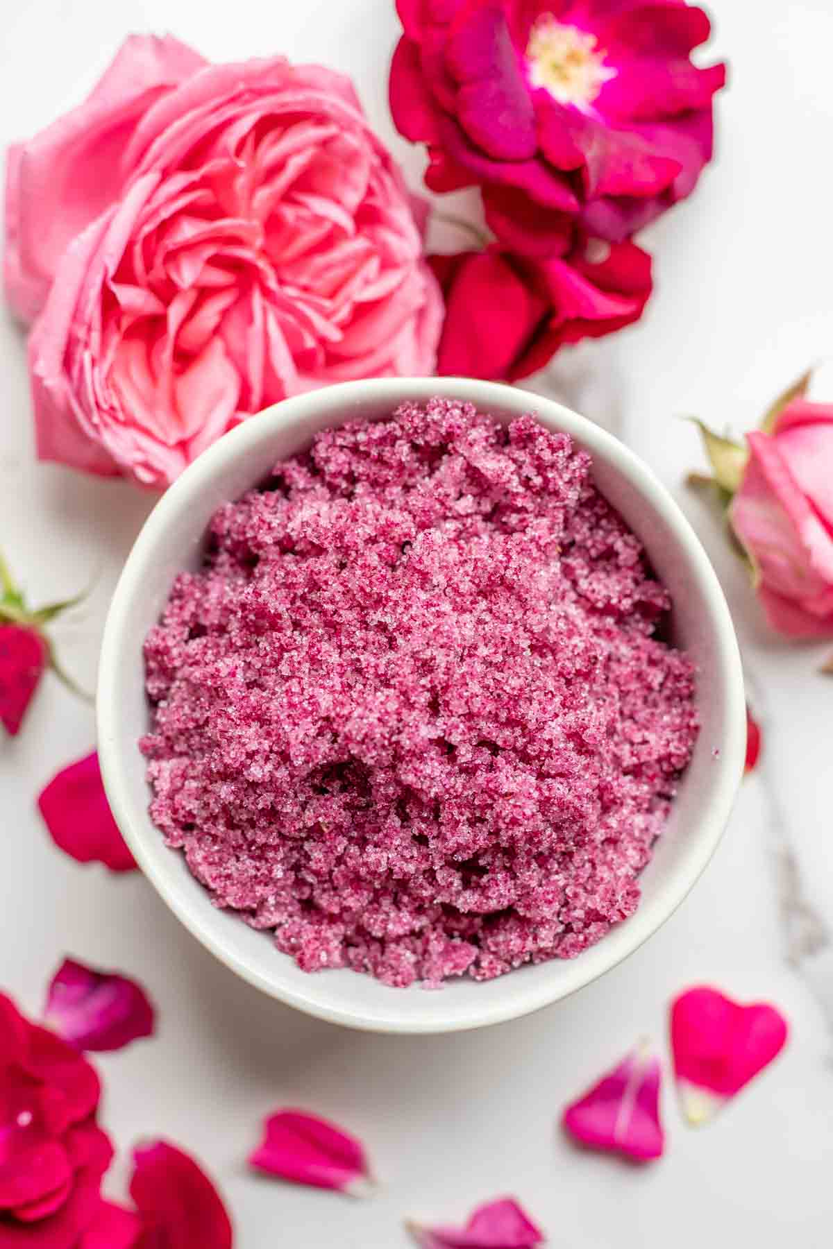 Rose sugar in a white bowl surrounded by roses.